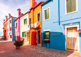 bright blue , red , orange and crimson colored picturesque buildings at a little street , houses of Burano with shadows in the evening and cloudy sky at background