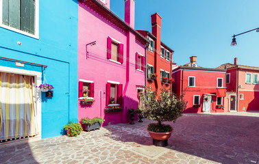 bright blue and crimson colored picturesque buildings at a little street , houses of Burano with shadows in the evening, Venice urban landscape