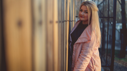 Obraz na płótnie Canvas A portrait of a beautiful girl, posing near a wooden fence at sunset in springtime.