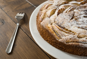 Homemade apple pie on the plate with a fork on the wooden background