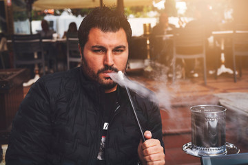 A Turkish Man is blowing smoke. He is actually smoking hookah.
