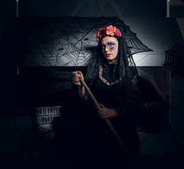 Attractive woman in dark dead bride role is posing for photographer with Halloween decorations.