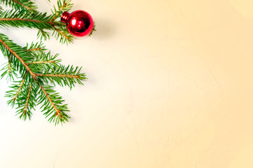 Christmas tree toy, red spherical shape lies next to a branch of spruce on a light yellow retro background