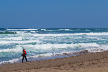 Fototapeta na wymiar Fisherman in helmet looking like astronaut standing and fishing on the beach next to the sea