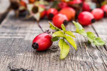 Red berries and rosehip leaves on a wooden table. C