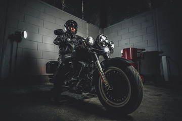 Obraz na płótnie Canvas In dark garage bearded biker on motorbike is posing for photographer on his bike.