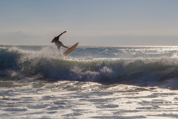 Unrecognizable surfer jumping over a wave, silhouetted against the sky at golden hour