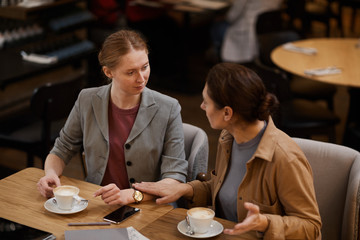 Two young businesswomen drinking coffee and discussing working moments during coffee break in cafe