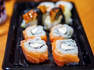Great selection of different kind of sushi on a black plate on a wooden table, Selective focus.