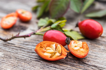 Red rosehips and cut berries in half with seeds on a wooden table.