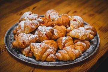 Big plate with a lot of delicious freshly cooked croissants. powdered sugar on top of croissants. Photo for restaurant or stand-up meal or banquet. Delicious tasty food at the party