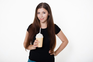 A young, beautiful girl in a black T-shirt and blue jeans is holding a glass with a straw in her hands. Studio photo on white background.
