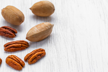 Pecans peeled and in shell lying on a white wooden surface, side view from above