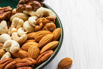 Assorted nuts on a green plate on a white wooden surface, side view from above