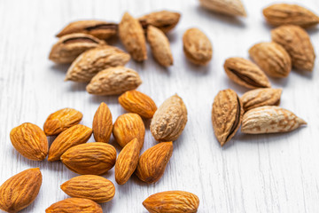 Almonds peeled and in shell lying on a white wooden surface, side view from above