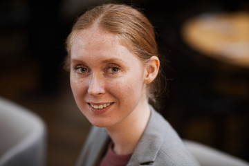 Portrait of red haired young businesswoman smiling at camera while sitting in cafe