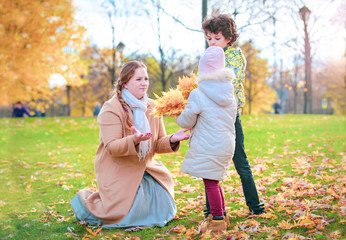 Two cute little baby and their mother having fun on beautiful autumn day. Happy children playing in autumn park. Kids gathering yellow fall foliage. Autumn activities for children.