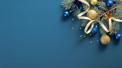 Christmas banner mockup with fir tree branches, golden ribbon, ball over blue background. Flat lay, top view, copy space. Winter holidays, New Year, Christmas concept