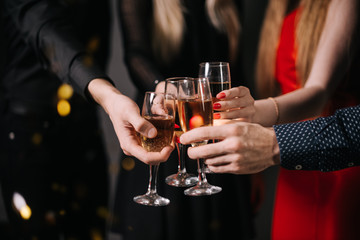 Close-up of man and woman hands clinking with champagne glasses. Four beautiful and cheerful friends in festive clothes on background.
