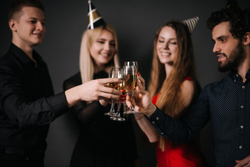 Four beautiful and cheerful friends are clinking glasses with champagne. Shooting in professional studio on isolated black background.