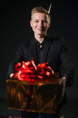 Man hands offer to take a gift in a colorful holiday package, close-up. Man dressed in a nice suit. Shooting in professional studio on isolated black background.