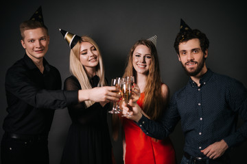 Group of cheerful young people areclinking with champagne glasses and celebrating new year. Shooting in professional studio on isolated black background.