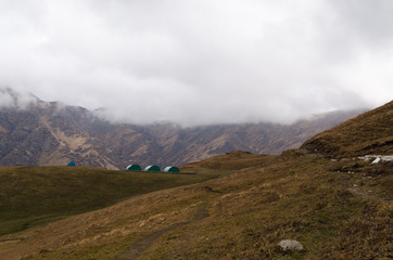 Fototapeta na wymiar Forest camp houses in the himalayan mountains with cloud covered brown mountains in the background