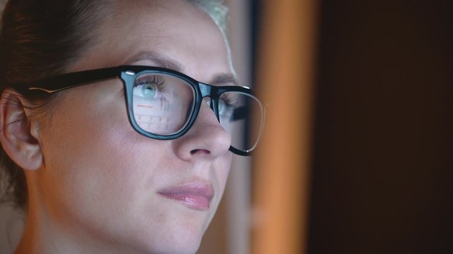 Woman in glasses looking on the monitor and surfing Internet. The monitor screen is reflected in the glasses