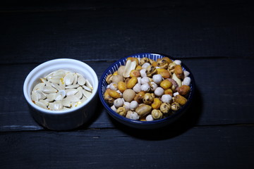 Nuts, seeds, peas, popcorn in a bowl on black wooden background