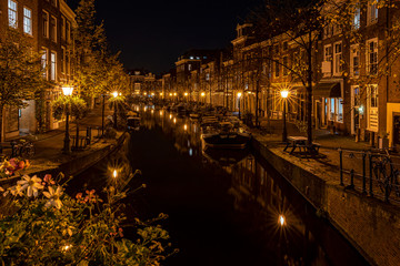 Fototapeta na wymiar A night shot from the Sint Jansbrug on the Oude Rijn with numerous boats and illuminated old canal-side houses, Leiden, the Netherlands