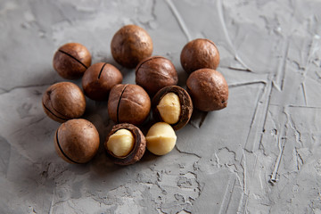 Obraz premium Pile macadamia nuts open kernels and shells on gray concrete background, top view