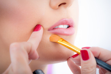 Makeup artist applying makeup on her face using powder brush