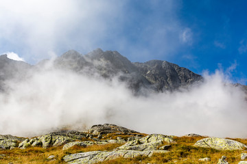 Mountain landscape in the autumn scenery. Clouds swirling in the valley, revealing only the upper parts of the peaks.