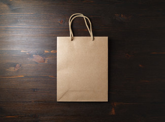 Blank brown paper bag with rope handles on wooden background. Flat lay.