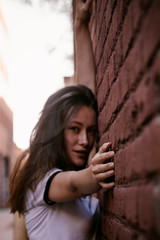 Woman with long hair on street. Red brick wall behind model. Street style fashion outfit. Urban lifestyle outfit. Plaid shirt, white t-shirt. Rebel girl. Showing different emotions. Sexy red lips.
