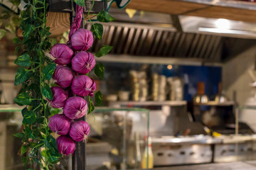 A bunch of red onions hanging on the background of the kitchen and steel utensils in a cafe or restaurant