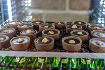 Round chocolate muffins in tartlets with hazelnuts in the middle stand in the refrigerator on a tray among coffee beans