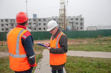 An engineer with a hard hat and helmet discussing a project at a construction site with a team leader in autumn or winter. architecture construction concept. Industrial safety