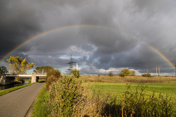 Wundersch&ouml;ner Regenbogen spannt sich &uuml;ber Naturlandschaft mit kleiner Stra&szlig;e