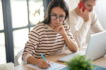 Wife wearing glasses feeling busy while filling tax declaration