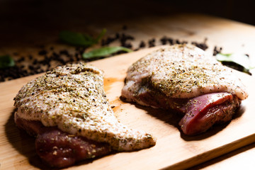 Two raw duck breasts with spices - majoram and thyme on the wooden cutting board in the kitchen. Pepper and leaves