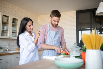 Dark-haired wife hugging husband slicing peppers for salad