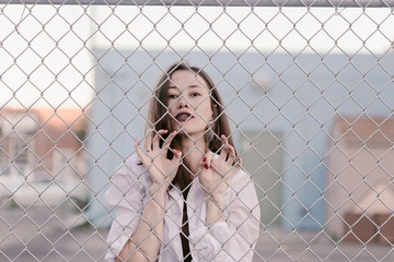 Pretty woman stands against wired fence. Model in white shirt. Purple lips. Pretty make up. Posing...