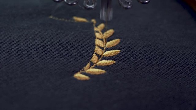 Extreme close up of Sewing needle moving at a very high speed, completing a golden wreath on black fabric.