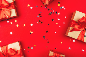 Several gift boxes with bows on a red background with confetti in the shape of stars. Holiday concept.