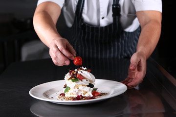 A cook in the kitchen is preparing Pavlov’s dessert. Bizet and fruit in a cooked dish. The concept of cooking from the chef.