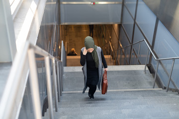 Fototapeta premium Woman wearing headscarf walking up stairs with briefcase