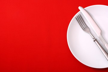 White plate with fork and knife on red table