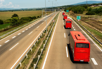 Caravan or convoy of red buses in line traveling on a highway country highway