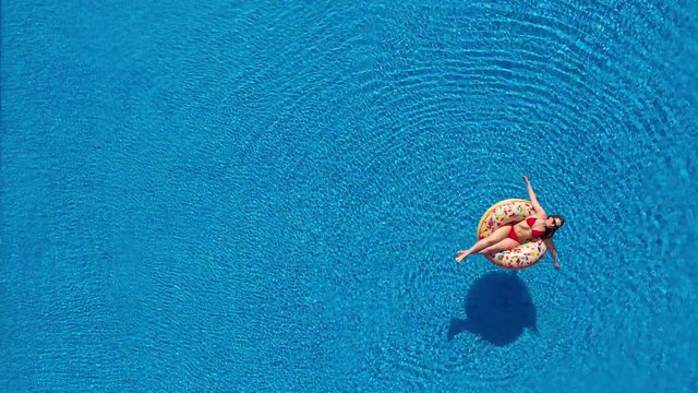 Aerial view of a woman in red bikini lying on a donut in the pool